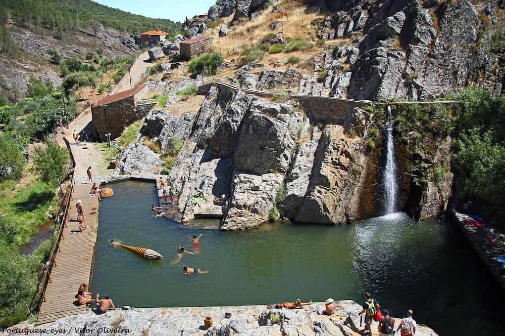 Piscina de água em granito com pequena cascata de água ao fundo, em volta estruturas rochosas 