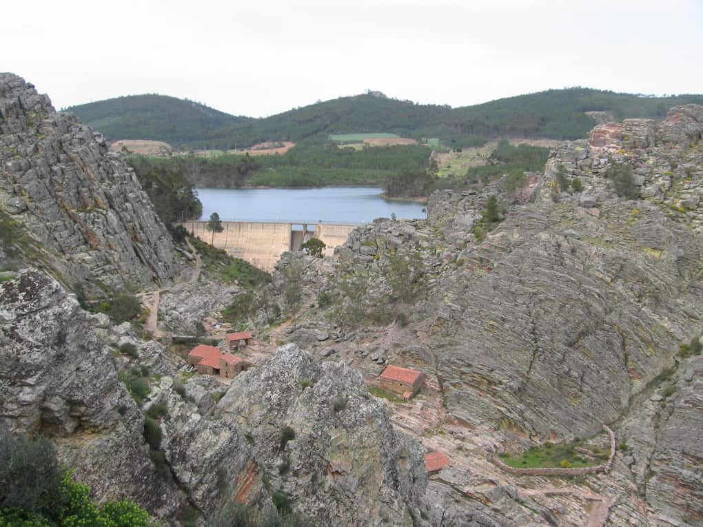 vale com moinhos ladeados por estruturas rochosas, terminando na barragem com rio.